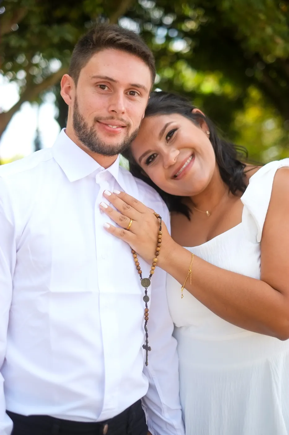 Retrato dos noivos de roupa branca, ela encostada nele com um terço na mão