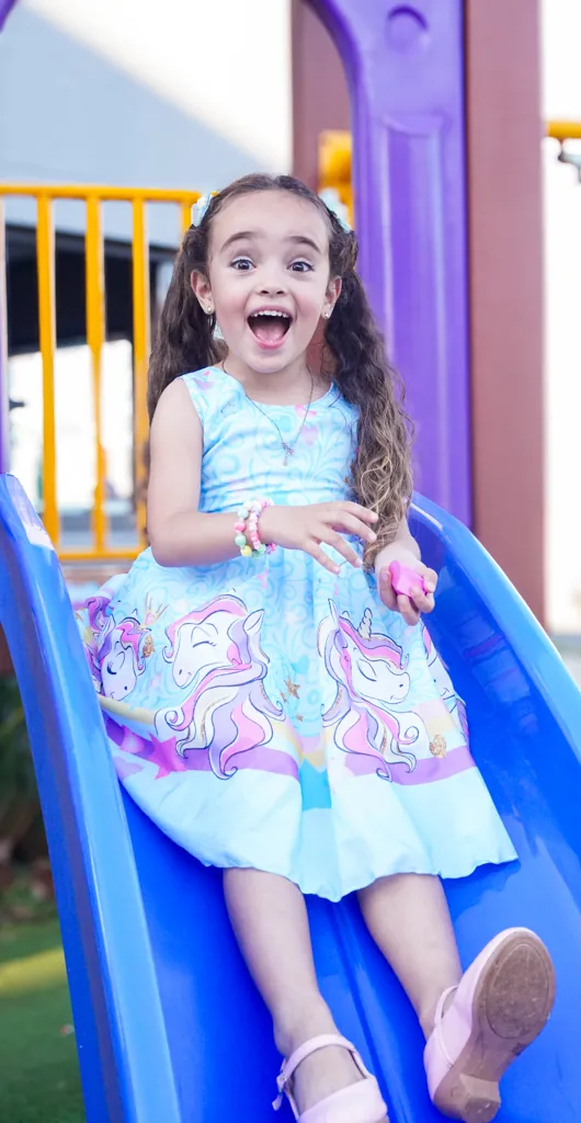 Menina sorrindo de surpresa ao descer em um escorregador azul