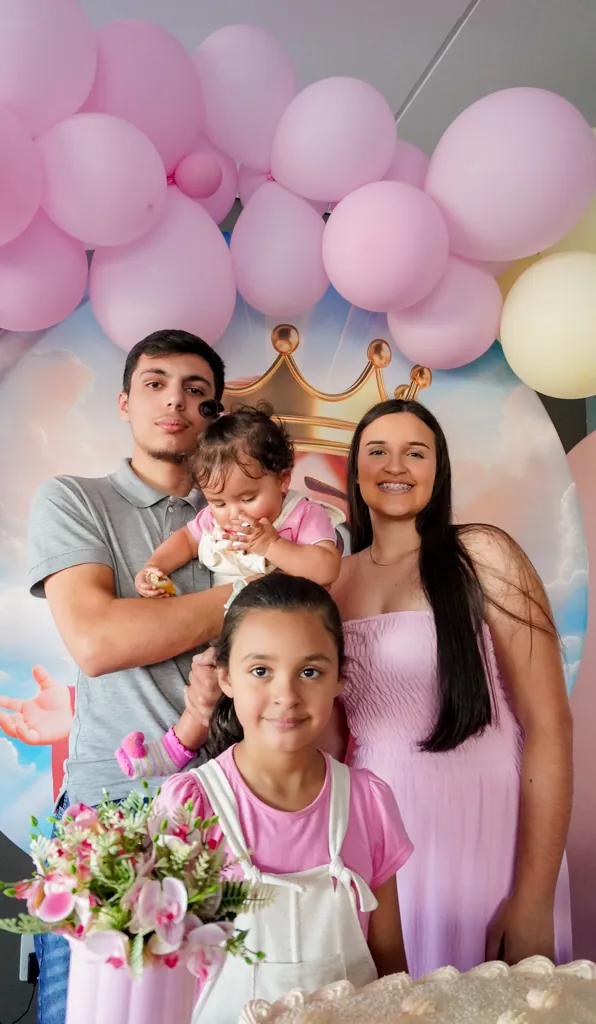 Família reunida em frente a um arco de balões rosa em uma festa