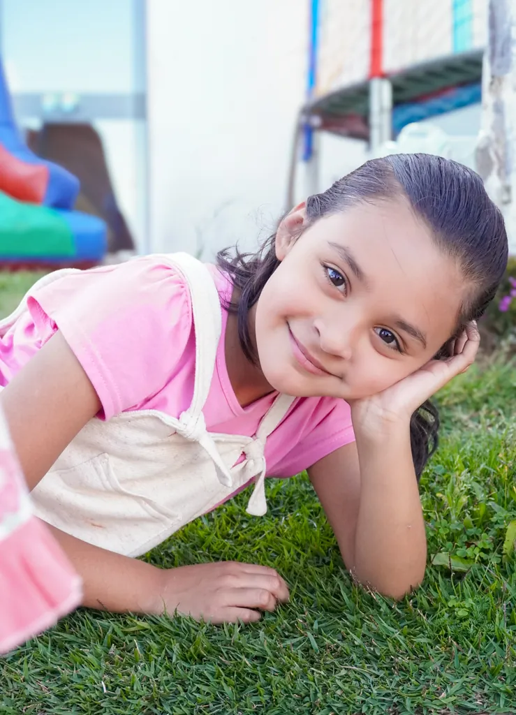 Menina deitada na grama, sorrindo com a mão no rosto