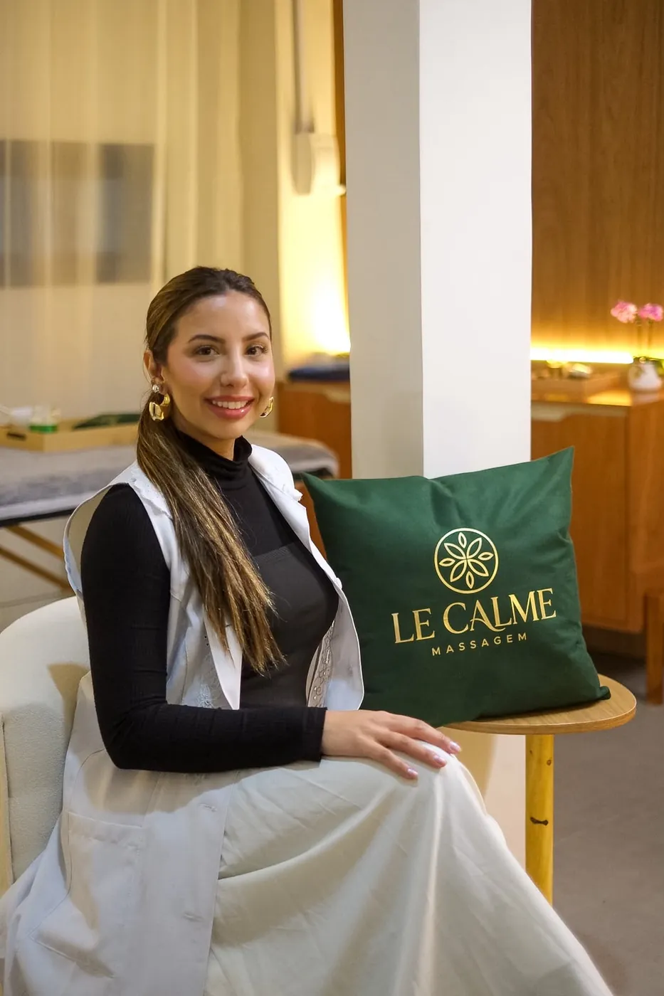Profissional sentada ao lado de uma almofada verde com a logo Le Calme Massagem