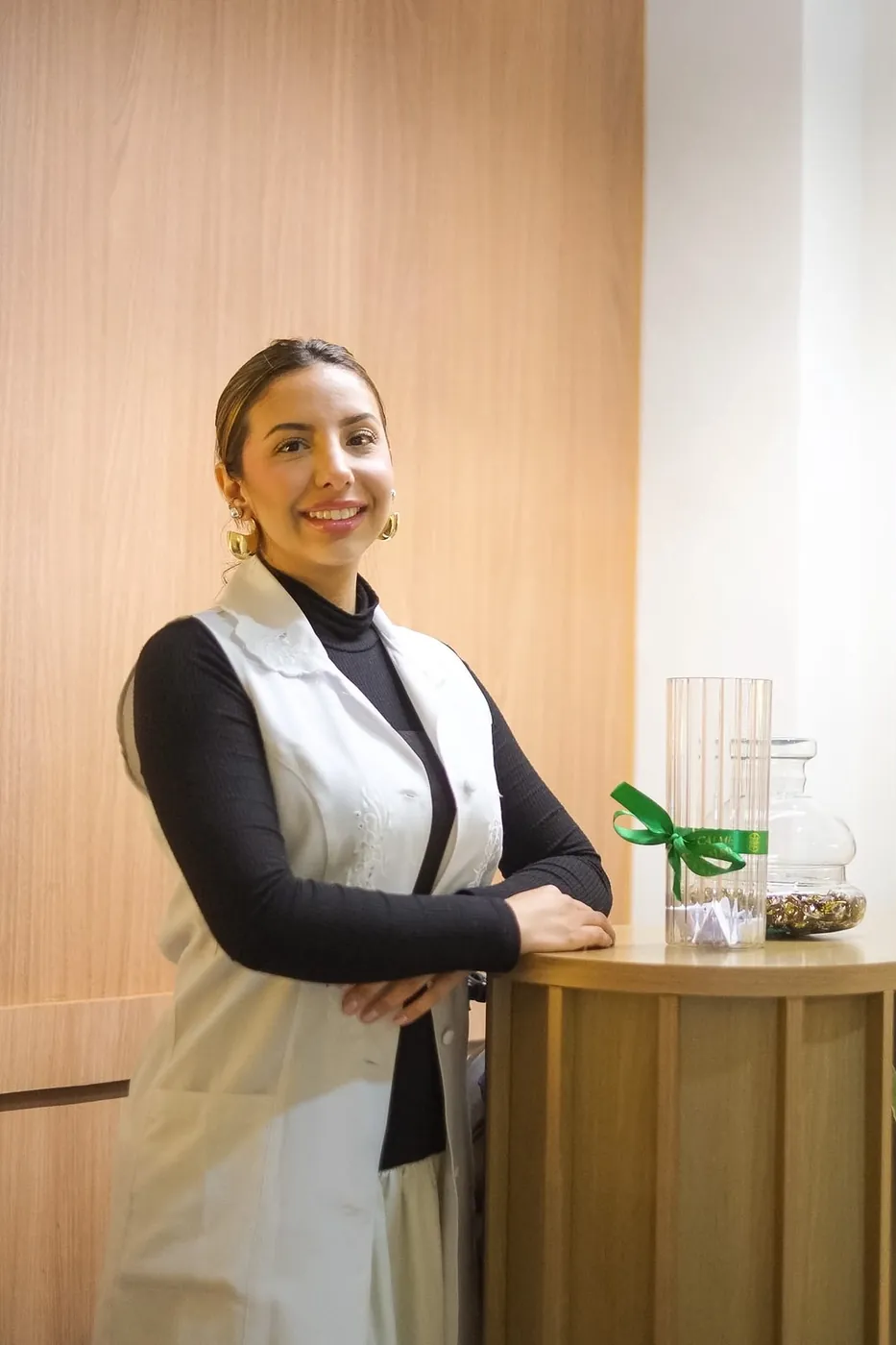Profissional sorrindo, apoiada em um balcão de madeira com laço verde