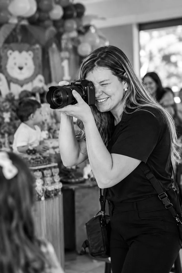 Fotógrafa do Arte em Clique sorrindo enquanto fotografa uma festa infantil, em preto e branco